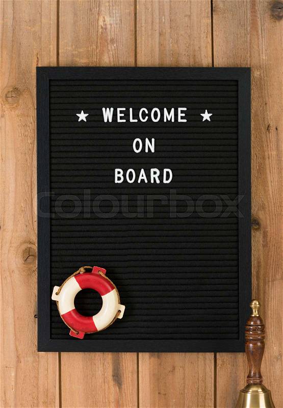 Welcome on board, phrase written on black felt message board with white plastic letters. Rustic wooden background, lifebelt and ship’s bell, stock photo