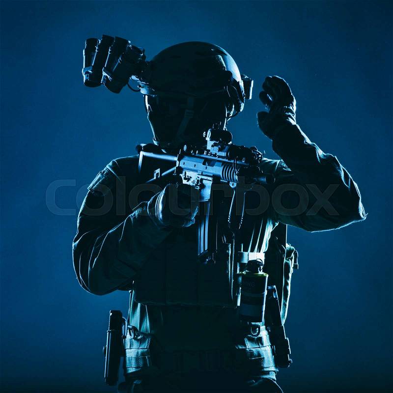 Special operations soldier, SWAT team fighter in mask and glasses, equipped night vision device, armed short barrel service rifle, looking back and showing freeze ..., stock photo