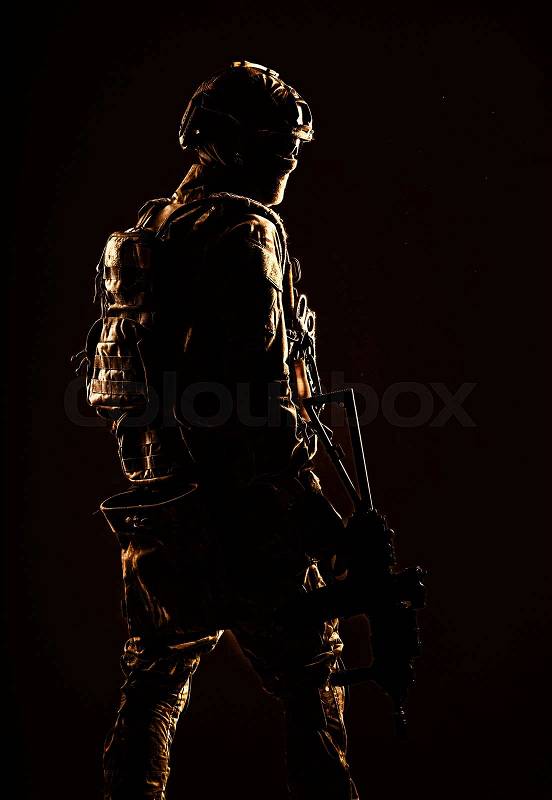 Low key studio shoot of army special forces soldier, commando fighter in mask, ballistic glasses, tactical helmet and battle uniform, holding short barrel service ..., stock photo