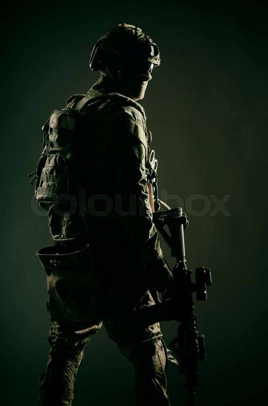 Low key studio shoot of army special forces soldier, commando fighter in mask, ballistic glasses, tactical helmet and battle uniform, holding short barrel service ..., stock photo