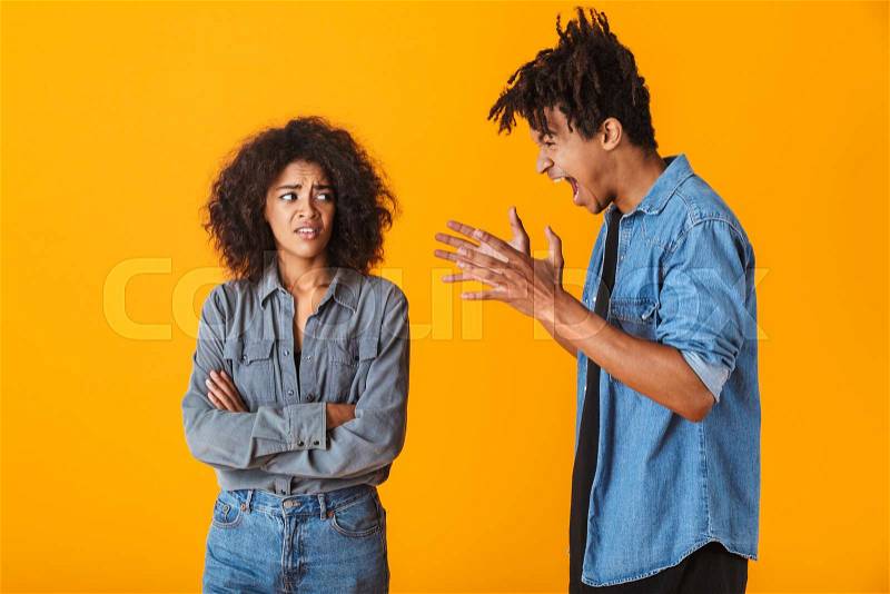 Young african couple standing isolated over yellow background, having an argument, stock photo