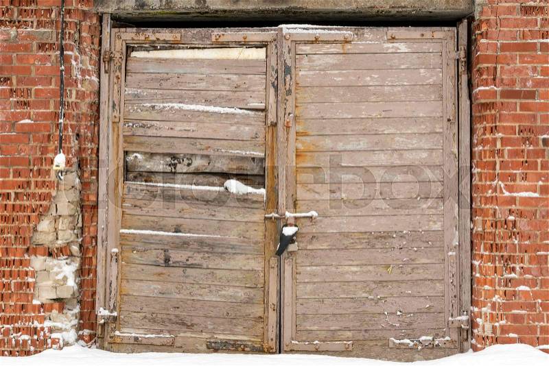 Old wooden door of abandoned garage with damaged brick wall, stock photo