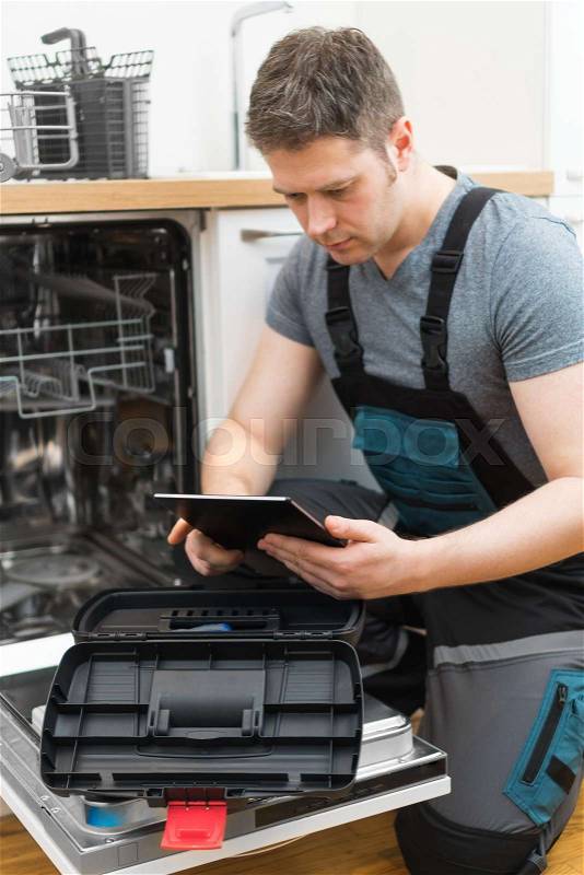 Handyman with tablet pc repairing domestic dishwasher in the kitchen, stock photo