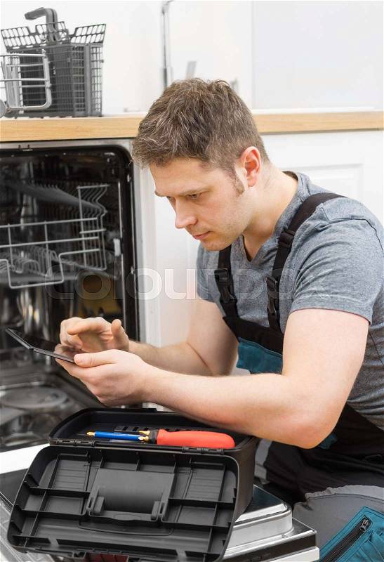 Handyman with tablet pc repairing domestic dishwasher in the kitchen, stock photo