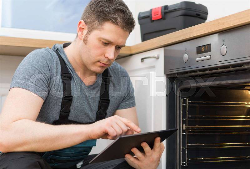 Handyman with tablet pc repairing domestic oven in the kitchen, stock photo