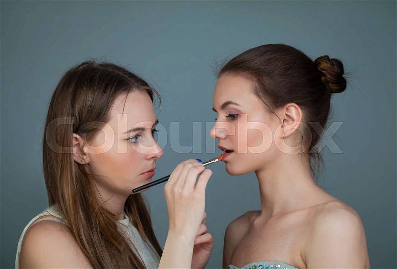 Woman makeup artist holding makeup brushes and applying lipstick on perfect fashion model lip, stock photo