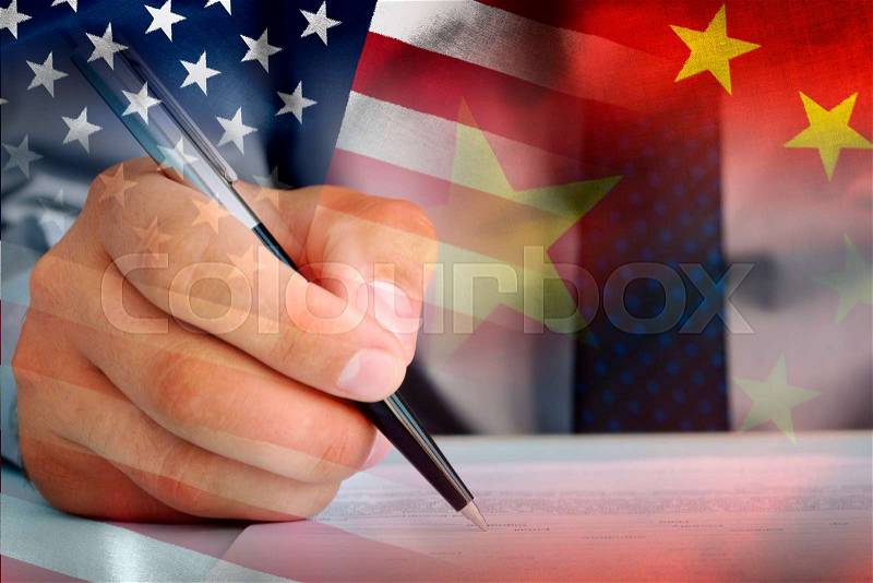 Official signing an agreement in a close up on his hand superimposed on the American and Chinese flags in a conceptual composite image, stock photo