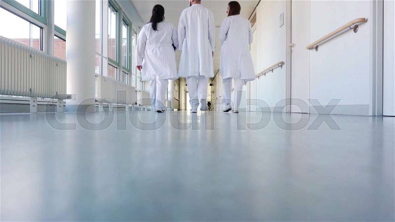 Three doctors walking down a corridor in hospital seen from behind, stock photo