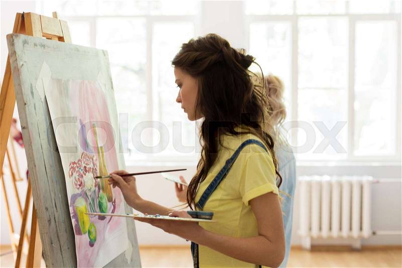 Art school, creativity and people concept - woman with easel, palette and brush painting at studio, stock photo