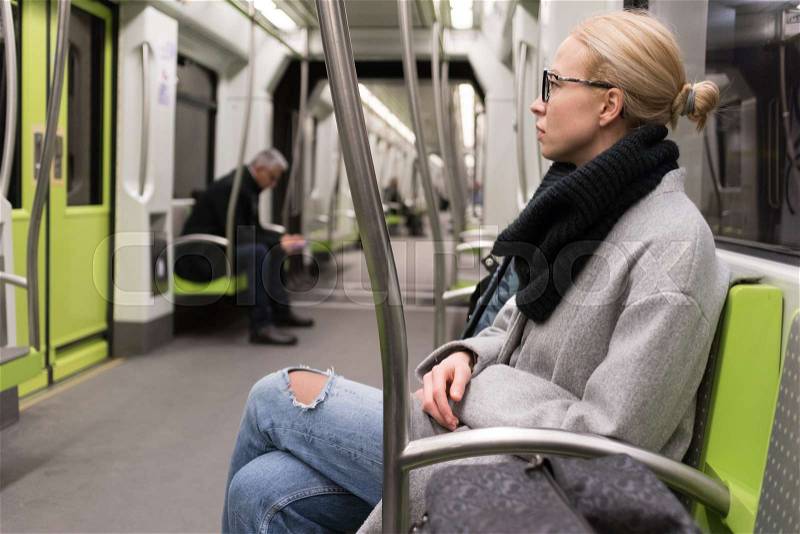 Beautiful blonde caucasian lady wearing winter coat and scarf traveling by metro. Public transport, stock photo