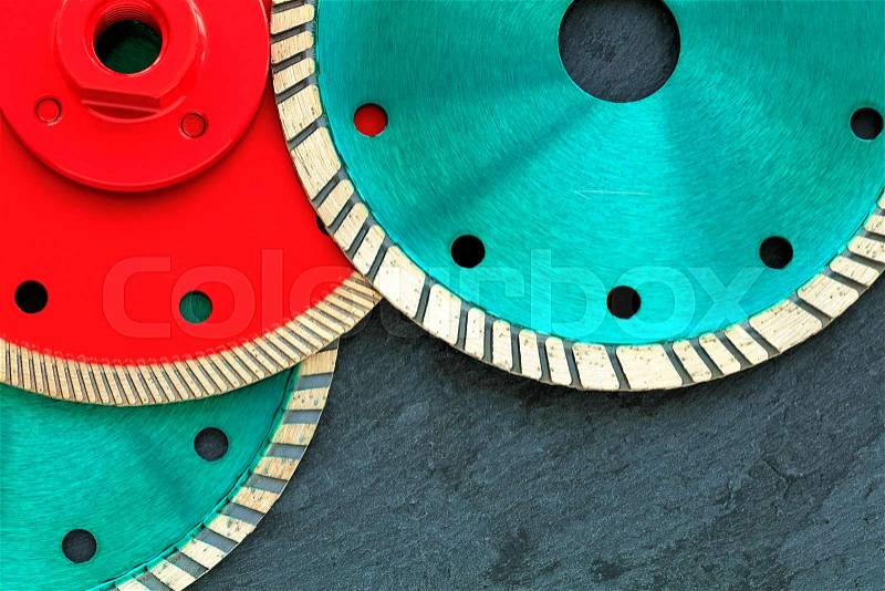 Several diamond cutting wheels of red and emerald color are located on top of each other against the background of gray granite close-up, stock photo