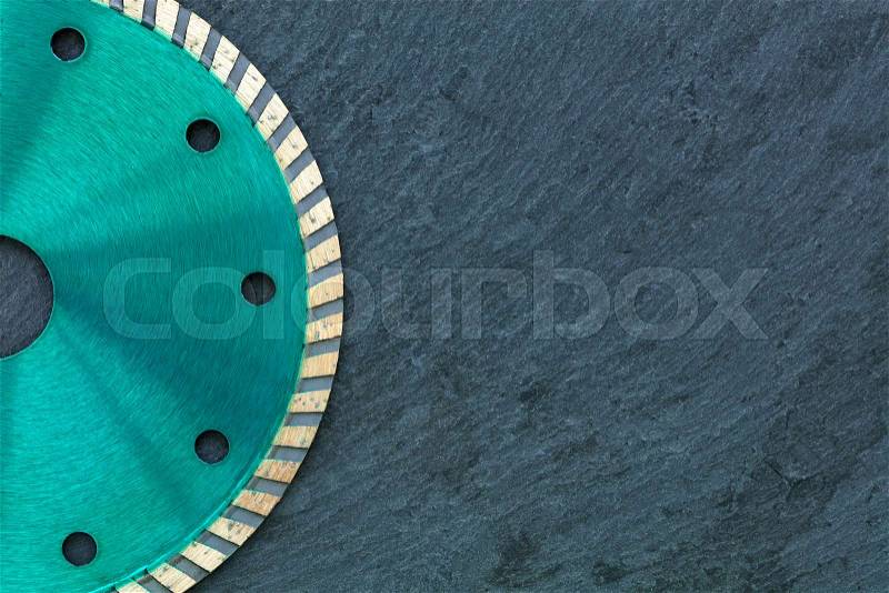 A part of the diamond cutting wheel of emerald color, on the right side of the copy space against a gray granite background close-up, stock photo