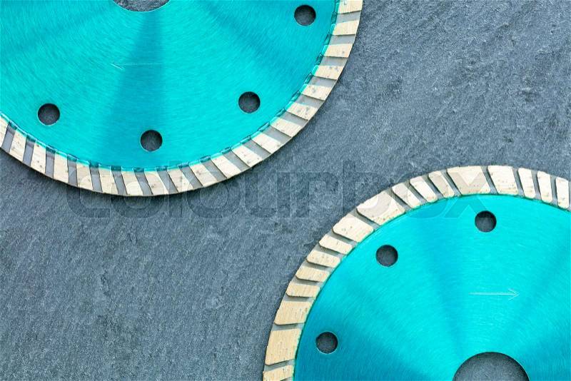 Part of the diamond cutting wheels of emerald color located diagonally relative to each other against the background of gray granite close-up, stock photo