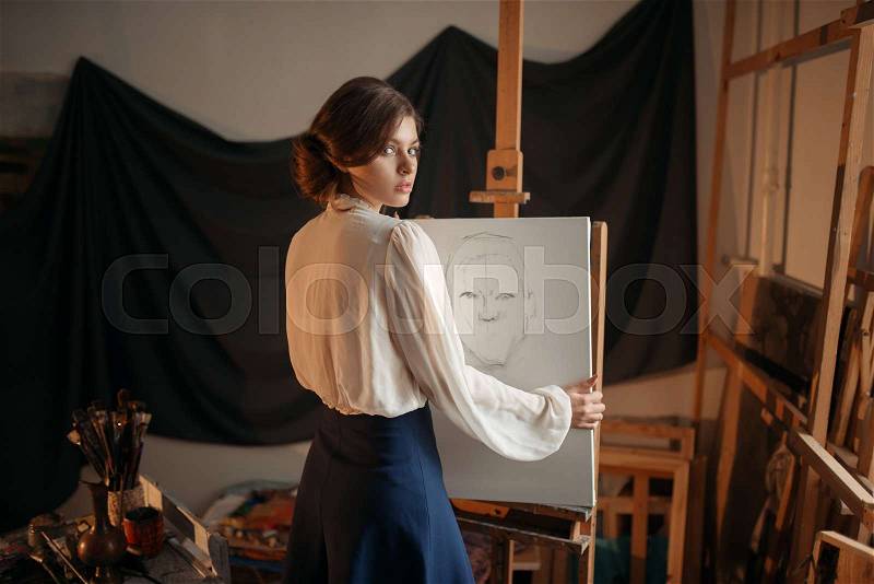 Cute female artist drawing in studio. Creative paint, pencil sketch on easel, workshop interior on background, stock photo