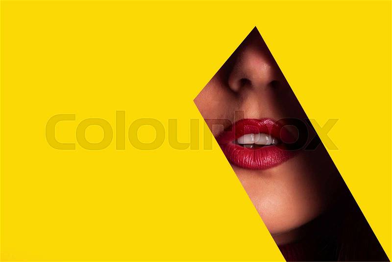 Girl with bright make up, red lipstick looking through hole in yellow paper. Make up artist, beauty concept. Ready to party. Cosmetics sale. Beauty salon advertising ..., stock photo