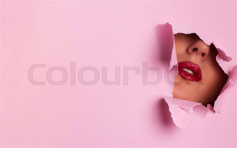 View of bright lips through hole in pink paper background. Make up artist, beauty cosmetics sale. Spring, woman day concept. Beauty salon advertising banner with ..., stock photo