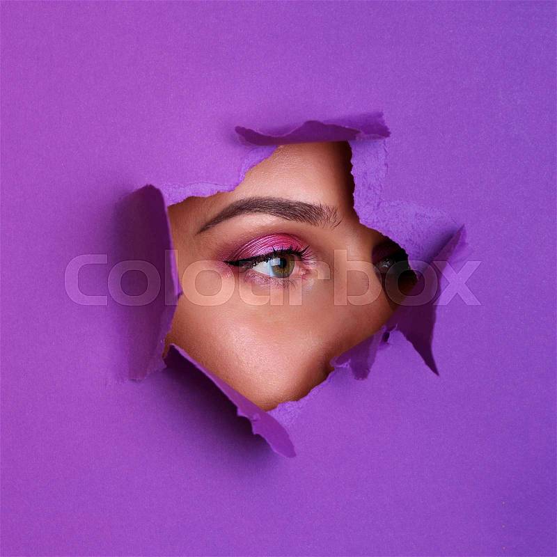 Beauty salon advertising banner with copy space. Beautiful girl looks through hole in violet paper background. Make up artist, fashion, beauty concept. Cosmetics ..., stock photo