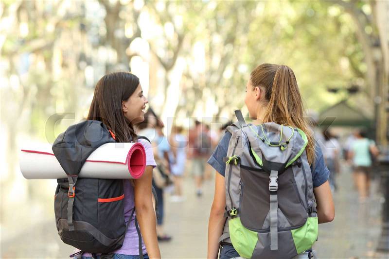 Back view of two happy backpackers walking in the street talking on vacation, stock photo