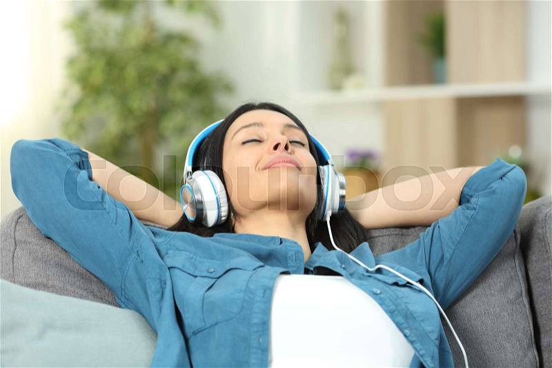 Relaxed woman resting listening to music sitting on a couch in the living room at home, stock photo