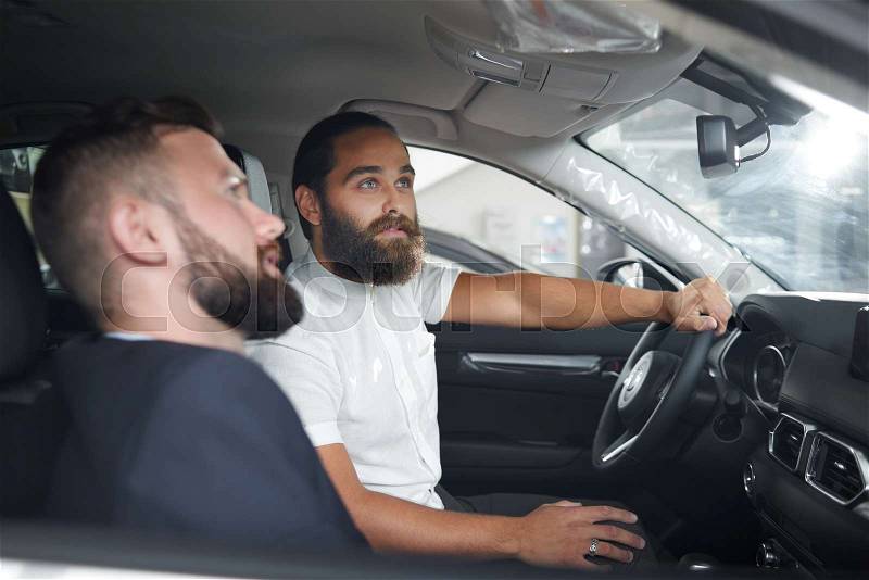 Car dealer showing to client car cabin. Handsome man in white shirt sitting on driver\'s seat, looking up and holding hand on steering wheel. Concept of car ..., stock photo
