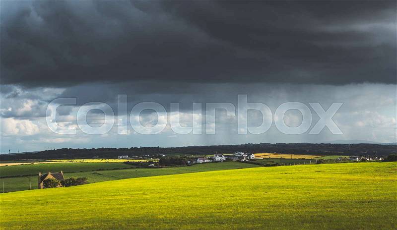 Grey rainy sky above the green meadow. Northern Ireland landscape. Dense dark clouds under the grassland and village. Stunning countryside Irish scenery. Horizon ..., stock photo