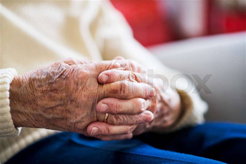 A close-up of a senior woman sitting and praying at home, hands clasped, stock photo