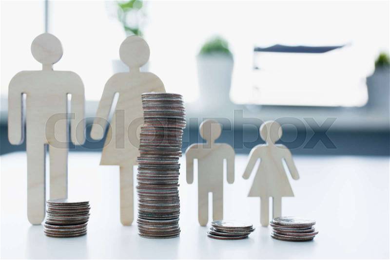 Wooden people silhouettes family with turrets of coins distribution budget and spending concept, stock photo