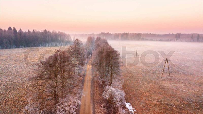 Rural misty dawn morning landscape. Aerial view of frozen road in early spring. Beautiful sunrise in Belarus, stock photo