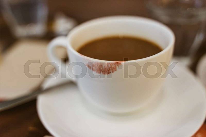 Close up of red lipstick smudges on hot latte in white coffee cup on wood table near window in coffee shop in the morning in vintage soft tone, metaphor of female ..., stock photo