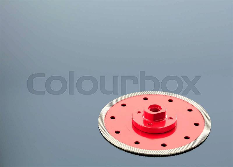 Diamond cutting wheel is red with a threaded nut, on the left side is a copy space on the mirror surface of a gray background with a slight gradient, stock photo
