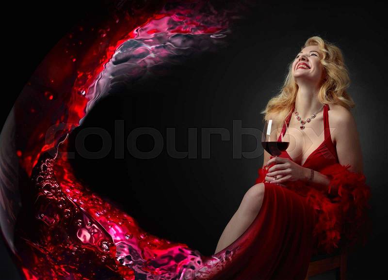 Attractive middle age woman in red evening dress with glass of red wine. Happy laughing forty years blonde with fluffy feather boa on a black background. Copy space, stock photo
