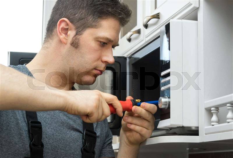 Male technician repairing microwave oven at home, stock photo