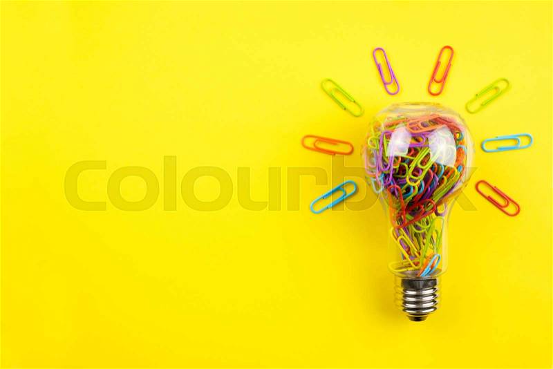 Light bulb filled with multicolor paper clips isolated on yellow background, stock photo
