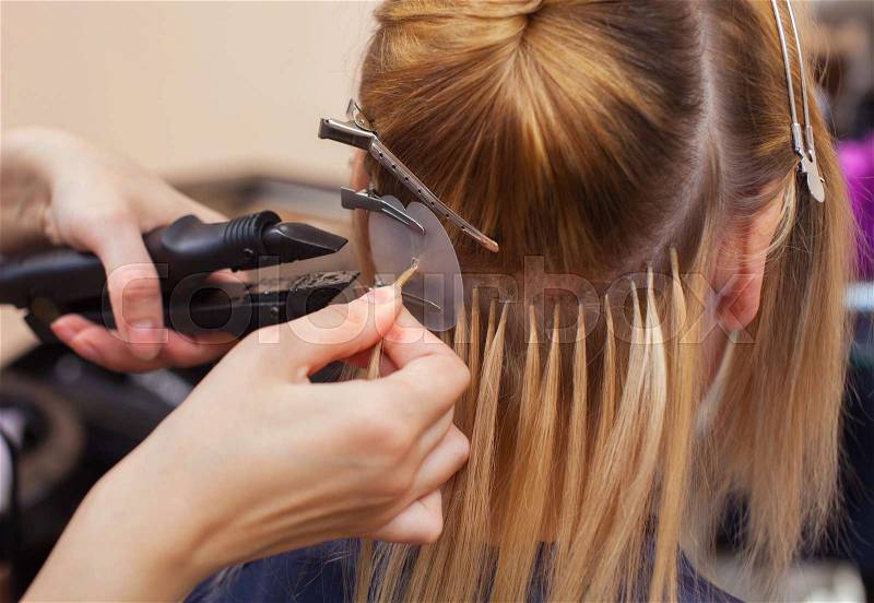 The hairdresser does hair extensions to a young girl, a blonde in a beauty salon. Professional hair care, stock photo
