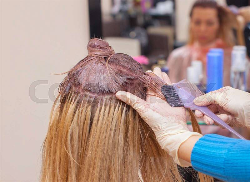 The hairdresser paints the woman\'s hair in white, apply the paint to her hair in the beauty salon, stock photo