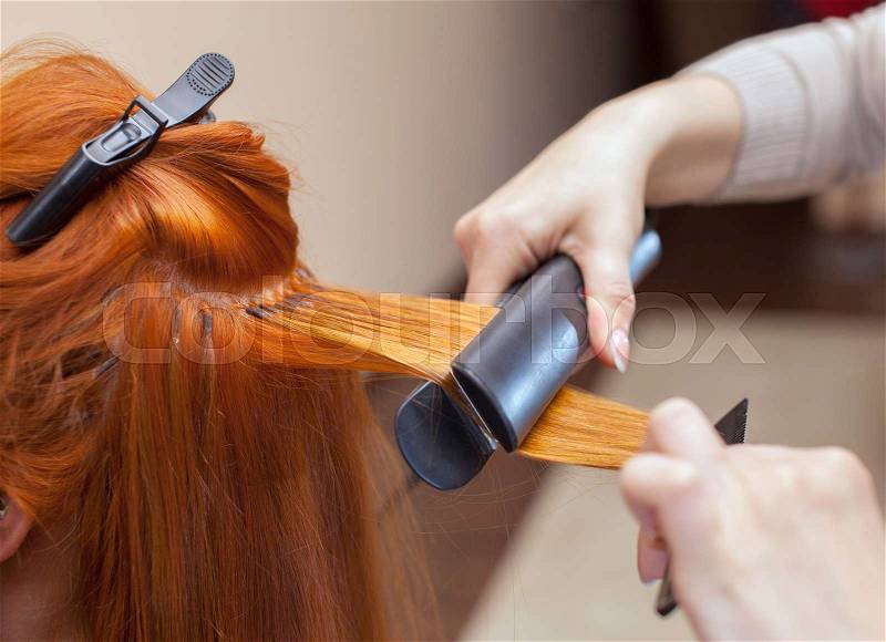 The hairdresser does hair extensions to a young girl, a redhead girl in a beauty salon. Professional hair care, stock photo