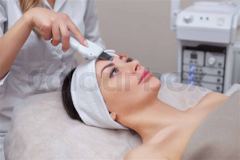 The doctor-cosmetologist makes the ultrasound cleaning procedure of the facial skin of a beautiful, young woman in a beauty salon. Cosmetology and professional skin ..., stock photo