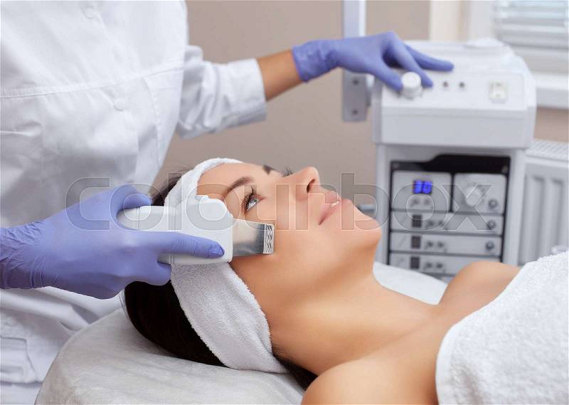 The doctor-cosmetologist makes the ultrasound cleaning procedure of the facial skin of a beautiful, young woman in a beauty salon. Cosmetology and professional skin ..., stock photo