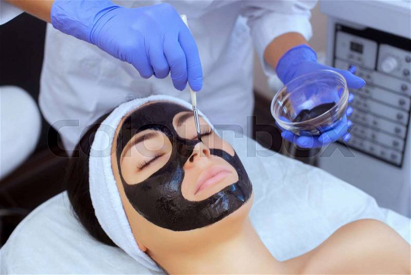 The procedure for applying a black mask to the face of a beautiful woman. Spa treatments and care of the cats in the beauty salon, stock photo