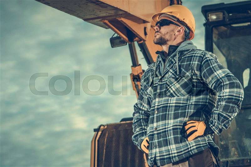 Excavation Work Supervisor. Caucasian Construction Worker Wearing Hard Hat and the Heavy Building Equipment, stock photo