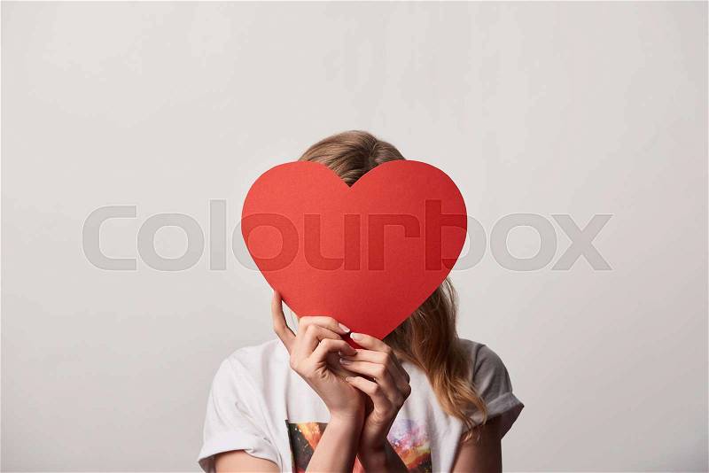 Young woman with obscure face and empty paper cut heart card isolated on grey, stock photo