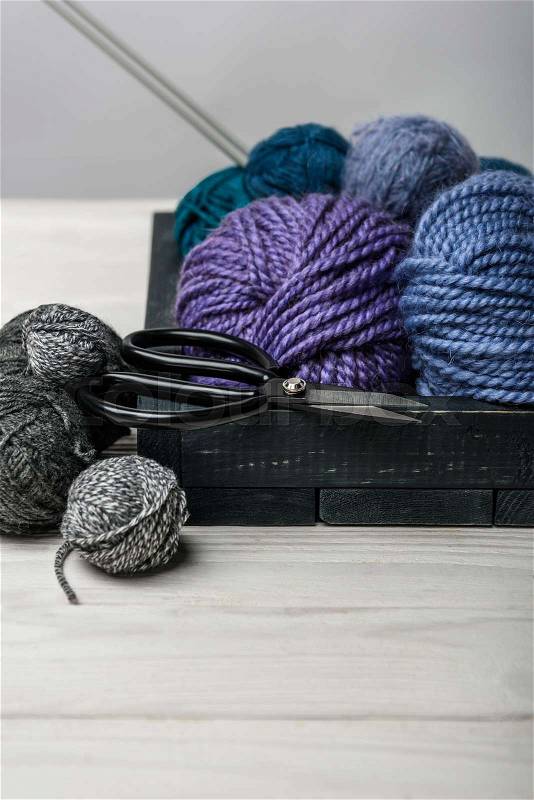 Close up view of yarn balls and scissors in wooden box on white tabletop, stock photo