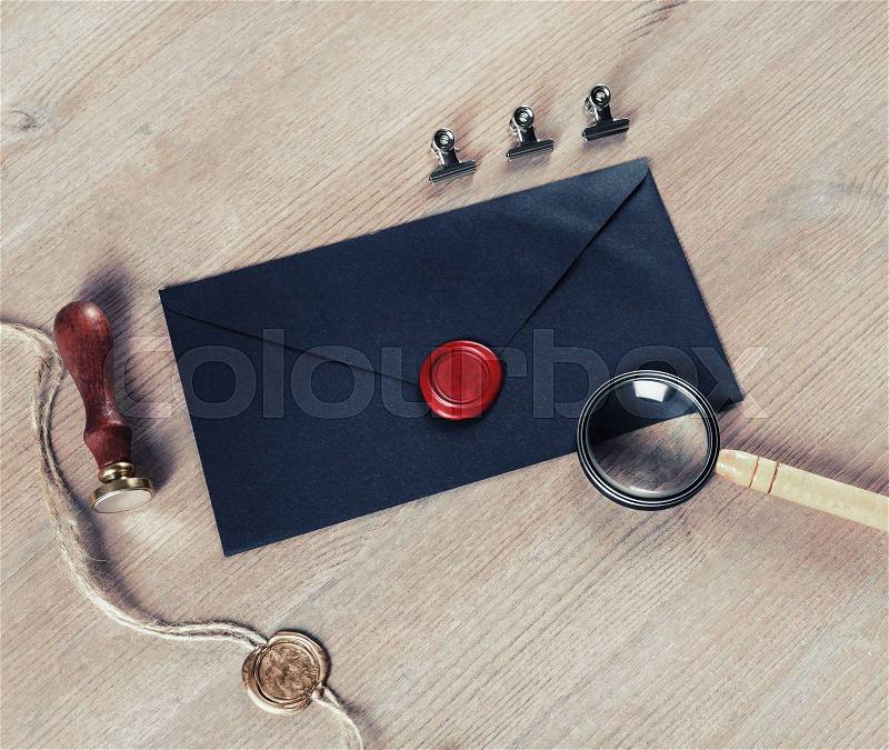 Old black envelope with red wax seal, magnifier and stamp on wooden background, stock photo