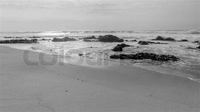 Beach windy morning wild ocean waves waters to horizon with rocky coastline cpntrasted black white landscape, stock photo