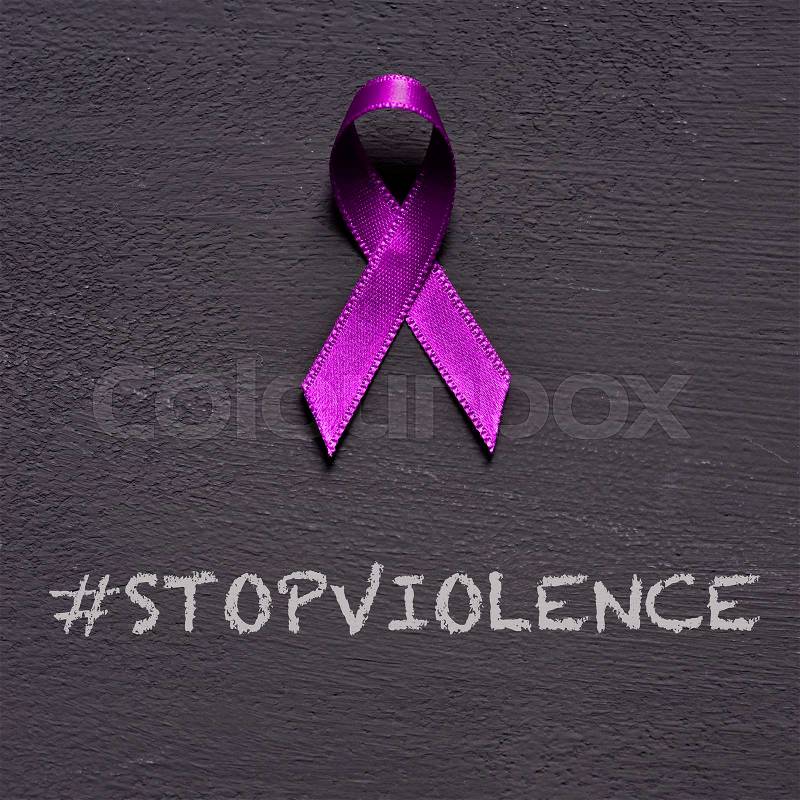 Closeup of a purple ribbon, for the awareness about the unacceptability of the violence against women, and the text stop violence on a dark gray background, stock photo