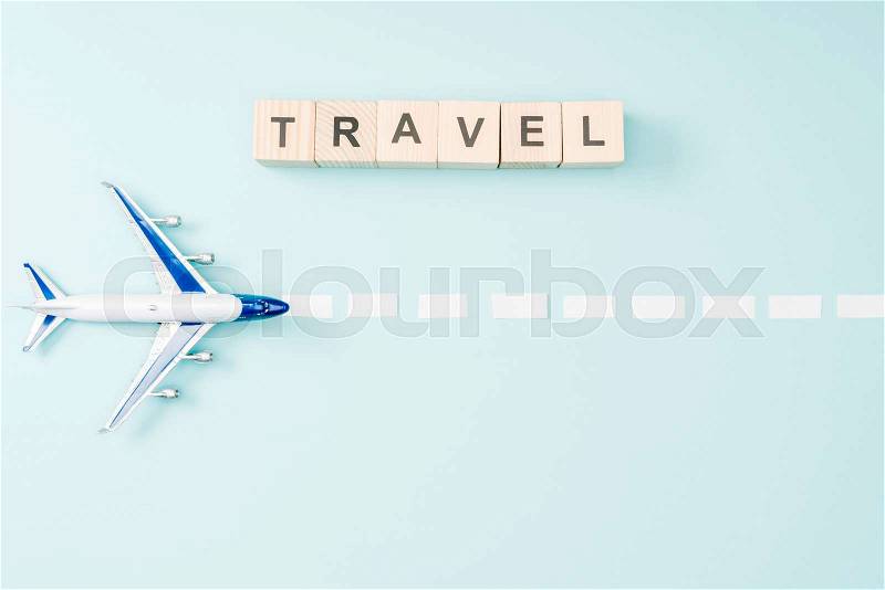 Top view of toy plane, dotted line and wooden cubes with travel lettering on blue background, stock photo