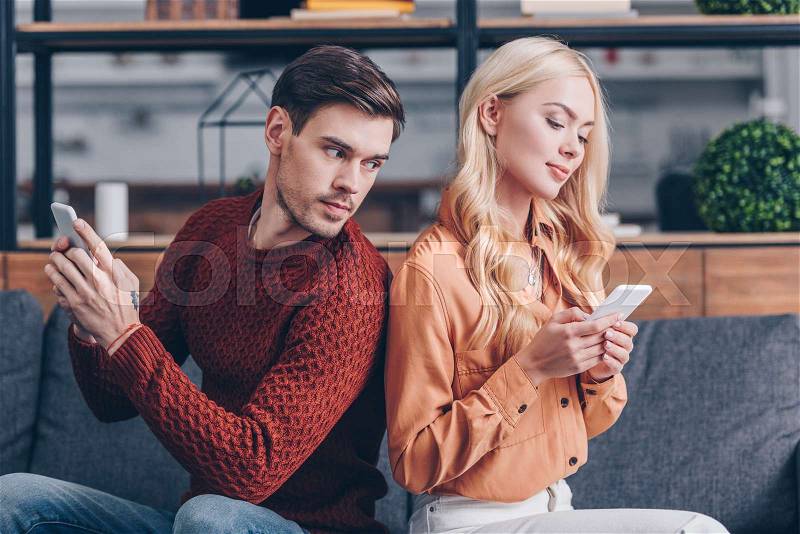 Young couple sitting back to back and using smartphones, jealousy concept , stock photo