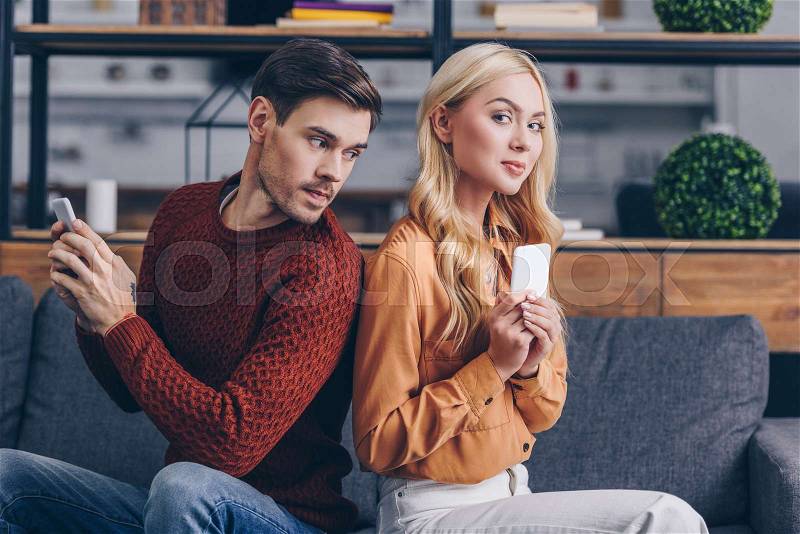 Young couple sitting back to back and using smartphones, mistrust concept , stock photo
