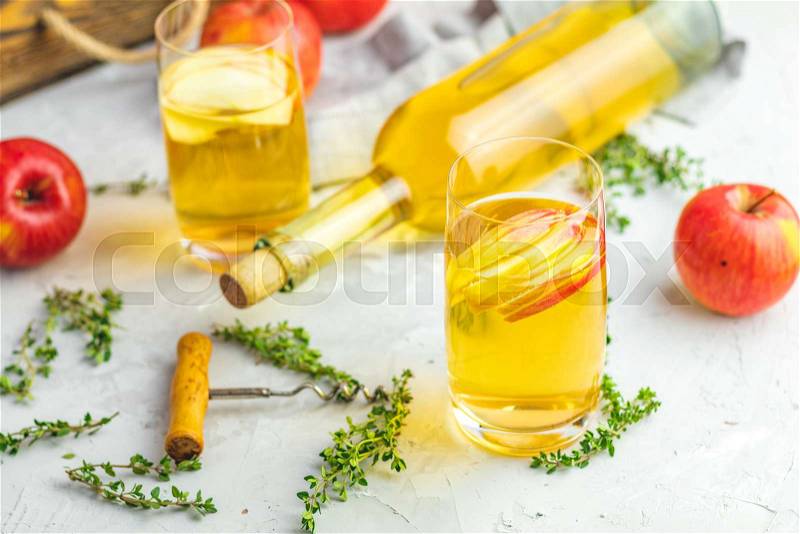 Bottle and glasses of homemade organic apple cider with fresh apples in box, light concrete table surface. Shallow depth of the field, stock photo
