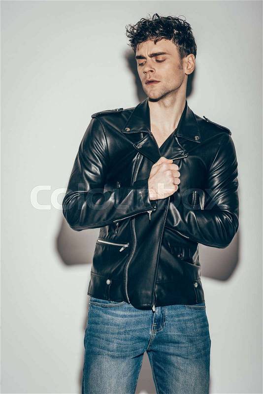 Handsome sexy man posing in black leather jacket on grey, stock photo